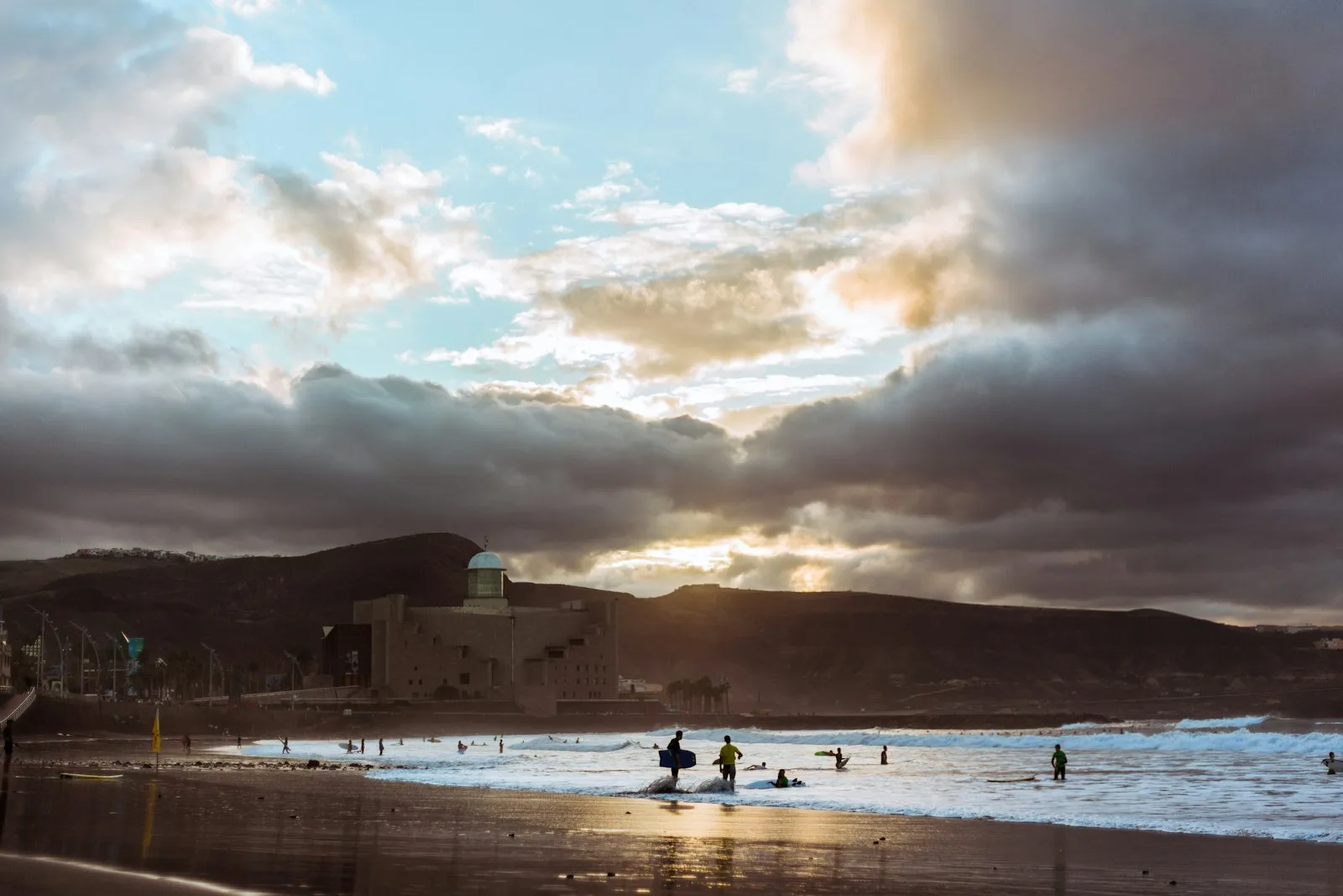 Personas nadando y haciendo surf en la playa de Las Canteras al atardecer, a un paseo de la terminal de cruceros de Las Palmas
